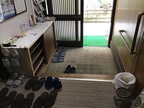 A room with a desk, various items on it, a pair of slippers on the floor, and a door leading outside. - Chatamago (Nagasaki)