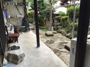 A concrete patio with a stone bench, a chair, and a table. There are plants and rocks in the background. - Chatamago (Nagasaki)