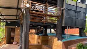 Una estructura de casa en el árbol de madera con una escalera y un pequeño cuarto cerrado.