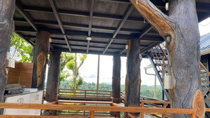 Una terraza de madera con barandilla de metal, una escalera y vistas al follaje circundante.