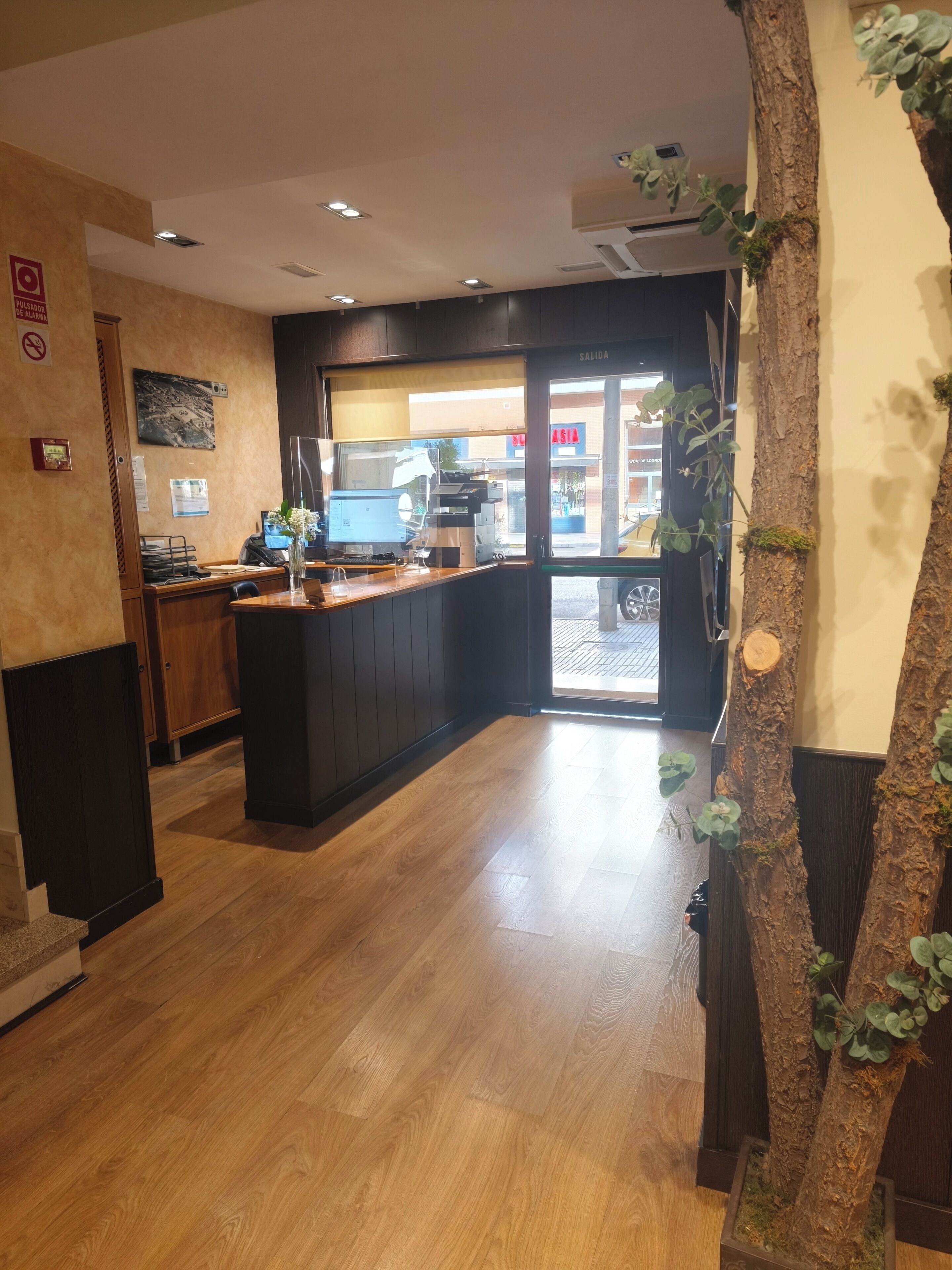 A reception area with a wooden floor, a reception desk, a computer, and a plant.