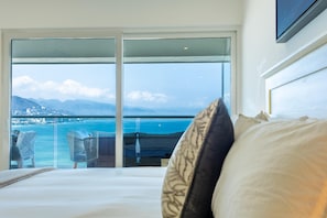 Ein Hotelzimmer mit einem großen Bett, Meerblick und einem Balkon mit Korbstühlen.
