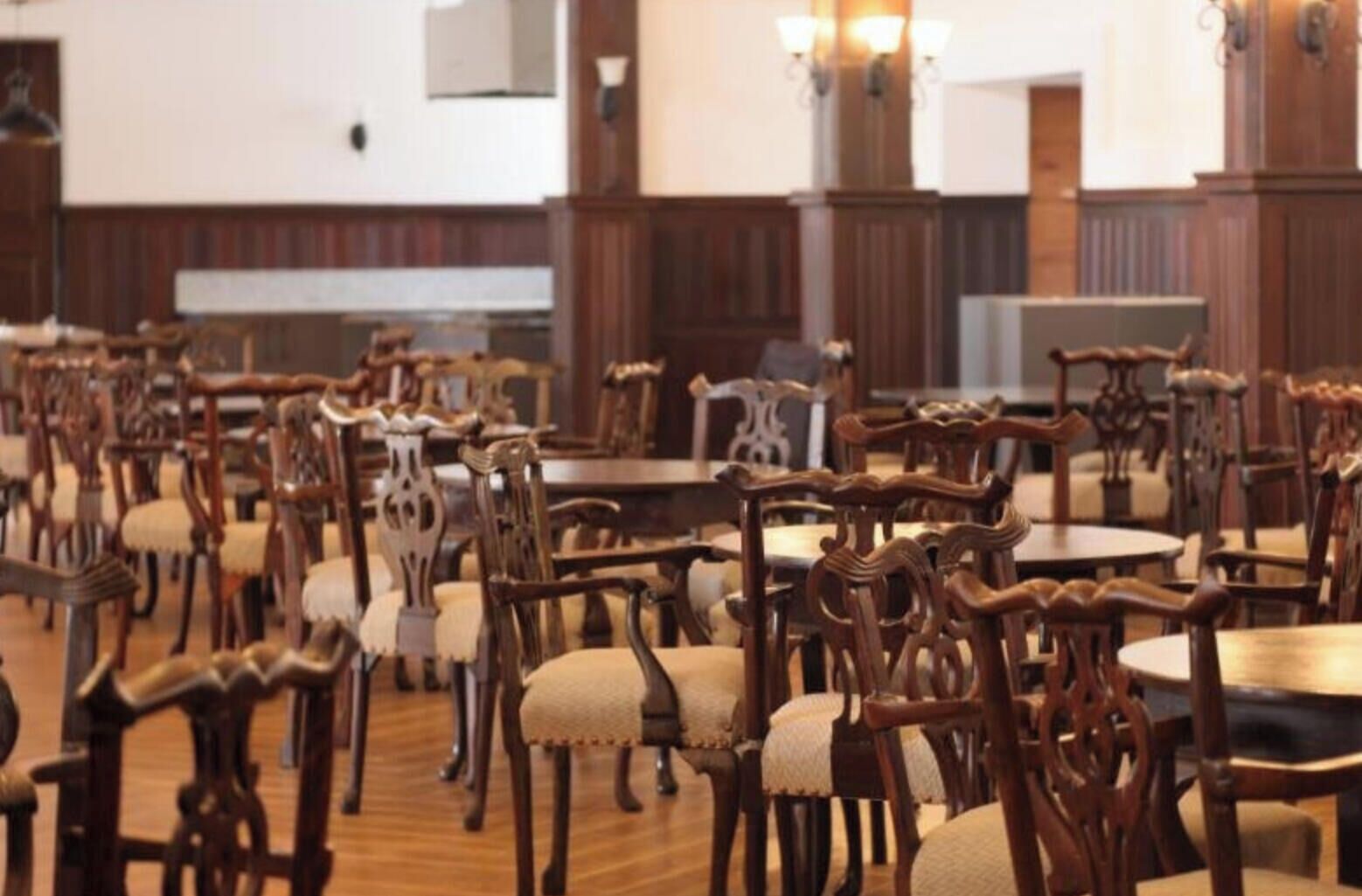 A dining area with multiple wooden tables and chairs, some with cushioned seats.