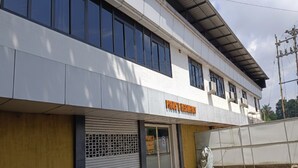 Un edificio de dos pisos con una persiana baja en la planta baja, un cartel que dice 'PIJOS & MESTERIA' y un porche cubierto en el nivel superior.