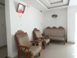 A room with two wooden chairs, a sofa, a ceiling fan, and a wall-mounted light fixture. - Hotel O Erumeli Bus Terminal Kottayam (Kanjirappally)