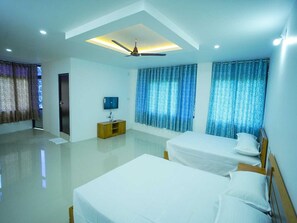 Habitación de hotel con dos camas, ventilador de techo, televisor y un mueble de madera.