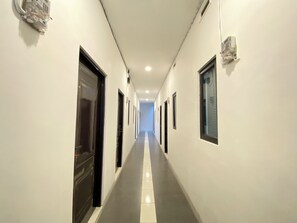Un pasillo largo y estrecho con puertas a ambos lados, iluminación empotrada y suelo de baldosas.