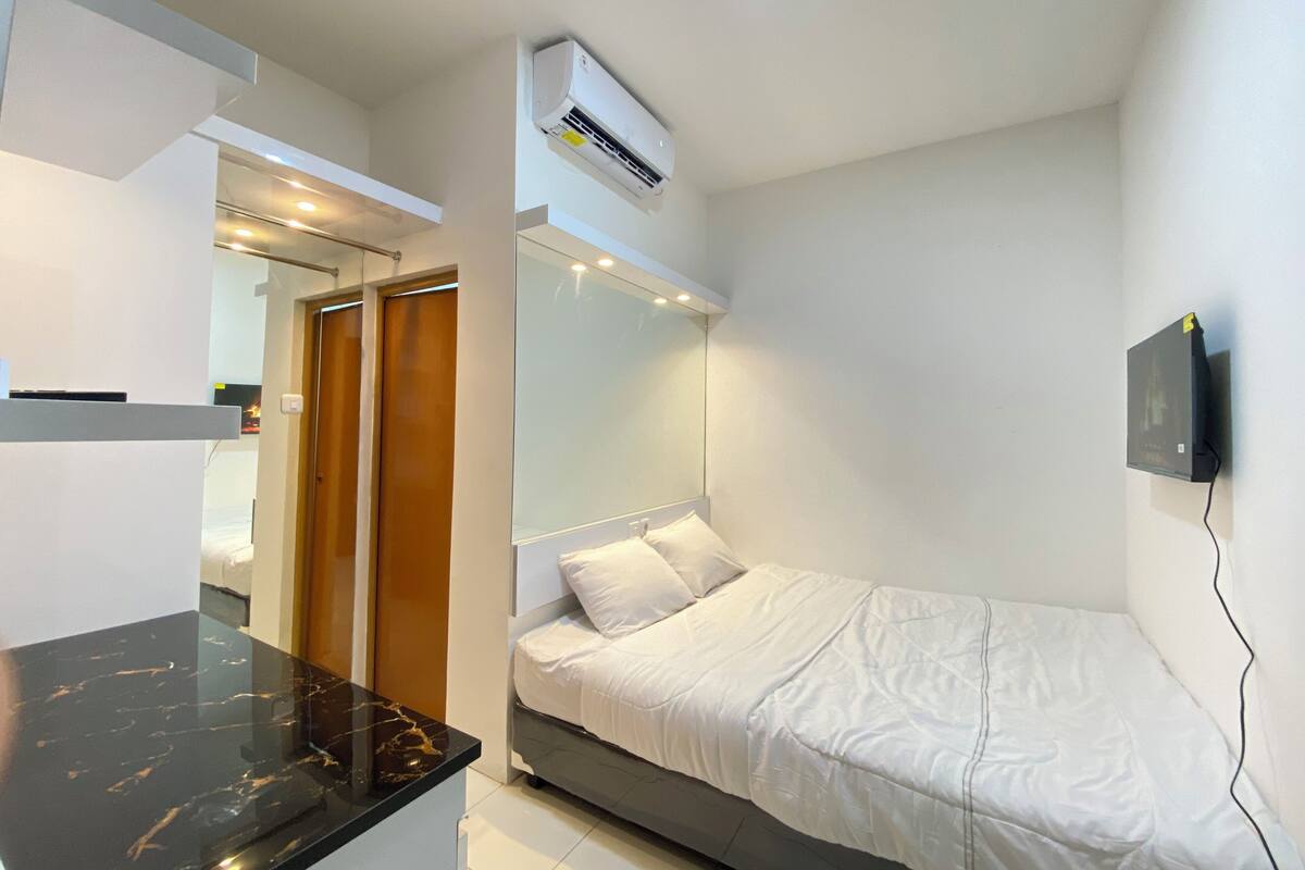 Un dormitorio con cama, espejo, aire acondicionado, televisor y una encimera negra.
