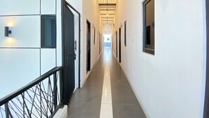 Ein langer, schmaler Gang mit Türen an beiden Seiten, einem Metallgeländer links und einer Decke mit eingelassenen Leuchten.