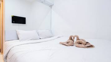 A hotel room with a bed, white bedding, a flat-screen TV mounted on the wall, and a pair of brown slippers on the bed.