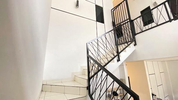 Eine Treppe mit schwarzem Metallgeländer, weißen Wänden und einem gefliesten Boden.