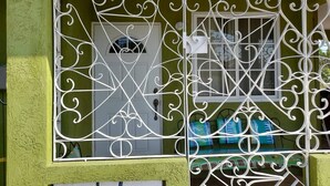 A window with decorative metal bars and a view of a room with a door and a window. - TJ Guest House - Jamaica (Spanish Town)