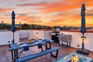 Eine Dachterrasse mit Esstisch, Grill und Feuerstelle.