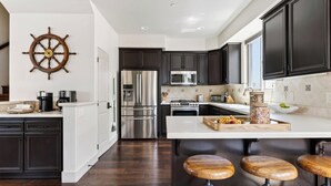 Eine moderne Küche mit dunklen Schränken, Edelstahlgeräten, einer Sitzecke mit Holzbarhocker und einer dekorativen Schiffsschwengel an der Wand.