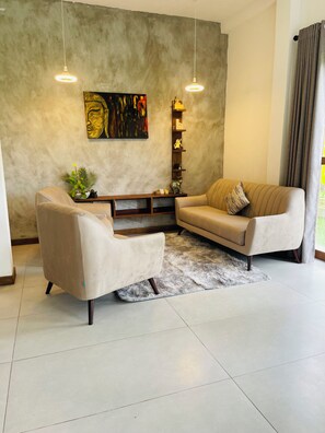 Una sala de estar moderna con un sofá, un sillón y una mesa de centro. Hay un cuadro en la pared y una estantería con objetos decorativos.