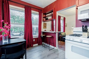 Una cocina compacta con estufa blanca, cortinas rojas, una pequeña barra y una mesa de comedor con sillas.