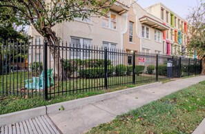 Un edificio residencial con valla metálica negra, un banco verde y un cartel de 'For Rent'.