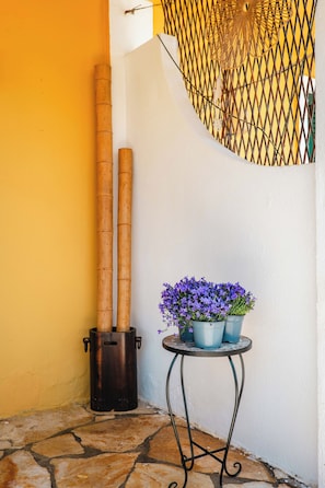 Una esquina con una planta de bambú, una mesa de metal con flores en macetas y una pared amarilla.