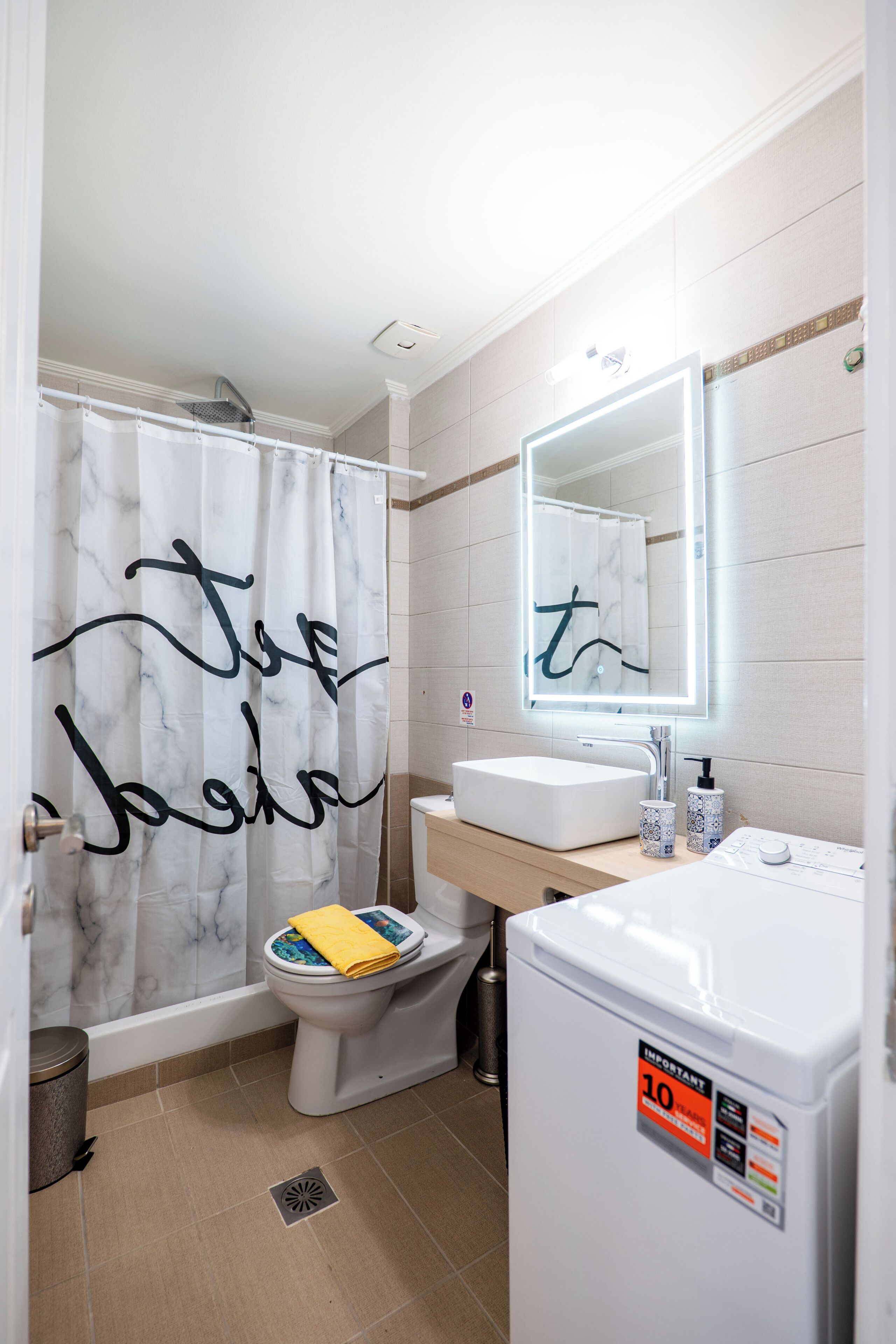 Une salle de bain avec un lavabo blanc, un miroir, des toilettes et un rideau de douche à motifs.