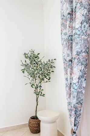 Un baño con un lavamanos blanco, una planta en maceta y una cortina de ducha con estampado floral.