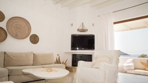 Een moderne woonkamer met een bank, een witte fauteuil, een ronde salontafel, een flatscreen televisie en een open haard.