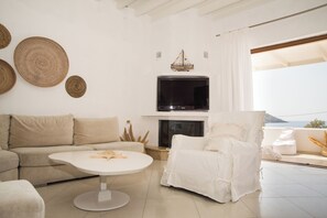 Uma sala de estar moderna com sofá, uma poltrona branca, mesa de centro redonda, televisão de tela plana e lareira.