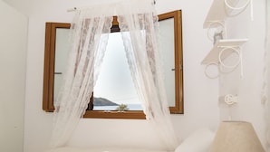 Een slaapkamer met een bed, een raam met uitzicht op zee en een nachtkastje met een lamp.