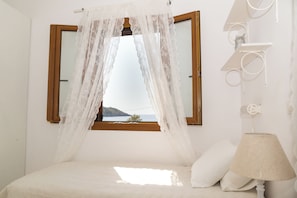 Quarto com cama, janela com vista para o mar e mesa de cabeceira com abajur.
