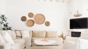 Een moderne woonkamer met een witte bank, een ronde salontafel en een tv aan de muur.