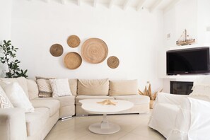 Uma sala de estar moderna com um sofá branco, uma mesa de centro redonda e uma TV fixada na parede.