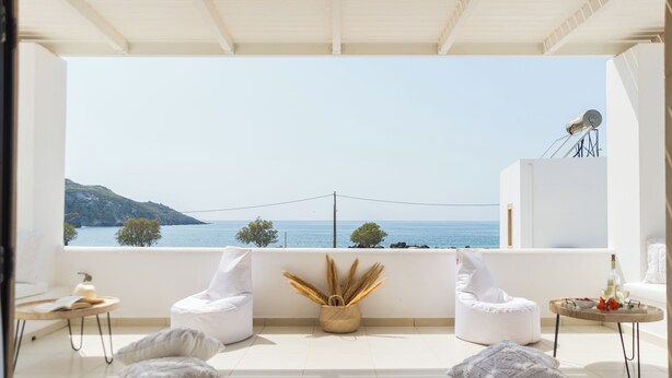 Een balkon met uitzicht op zee, wit meubilair en een mand met gedroogde planten.