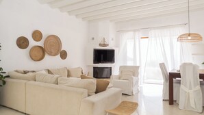Een moderne woonkamer met een bank, stoelen, een televisie en decoratieve geweven objecten aan de muur.