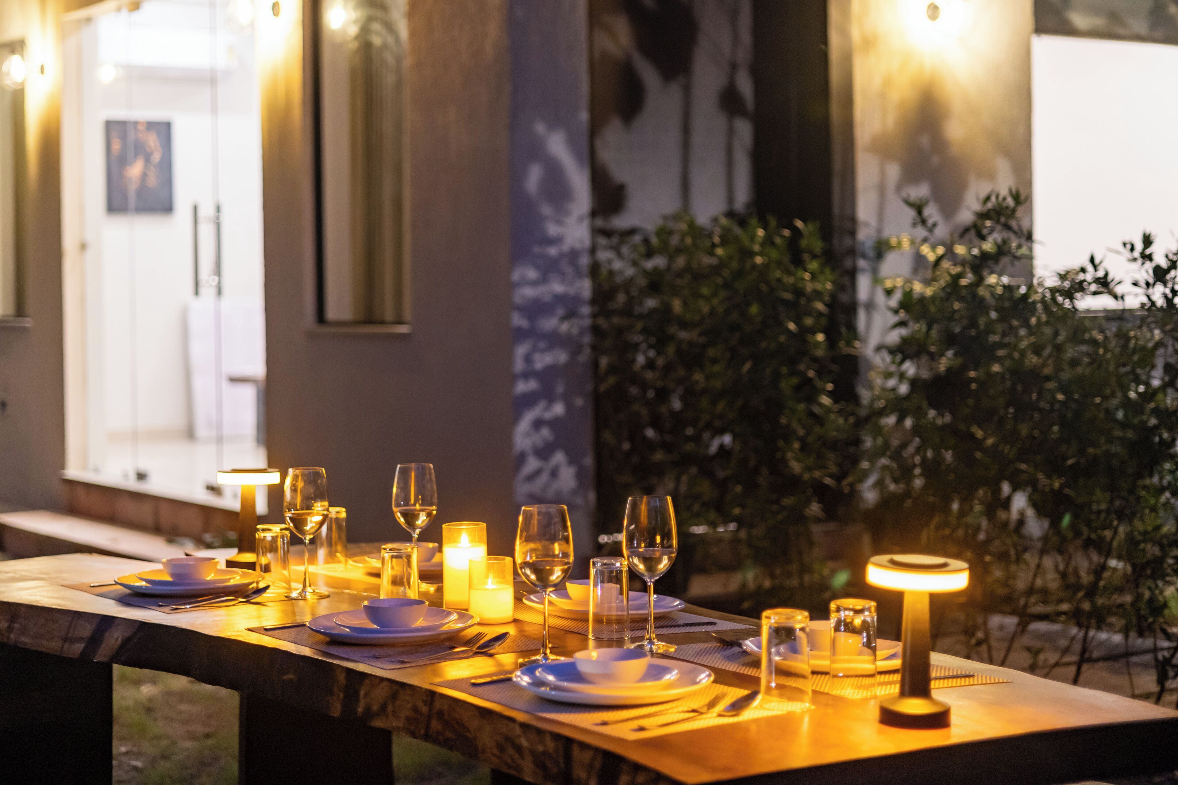 Una mesa de comedor dispuesta con velas, copas y platos, evocando una cena romántica al aire libre.