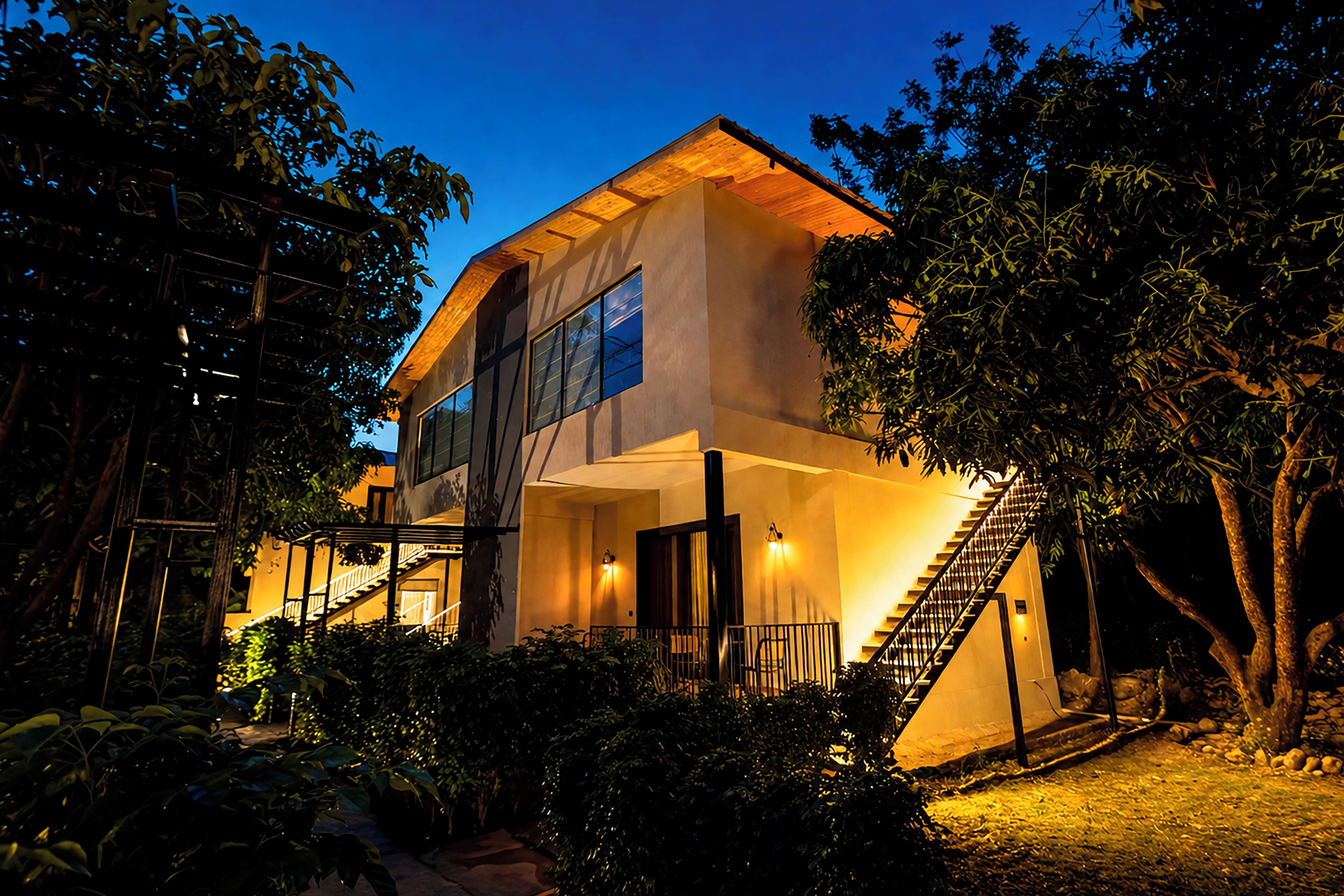 A modern two-story house with a staircase, large windows, and a well-lit exterior.