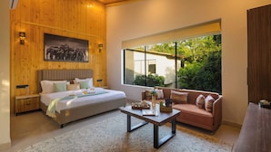 A modern bedroom with a bed, a sofa, a coffee table, and a large window. - Sylvaara Suites by ELIVAAS Jim Corbett (Ramnagar)