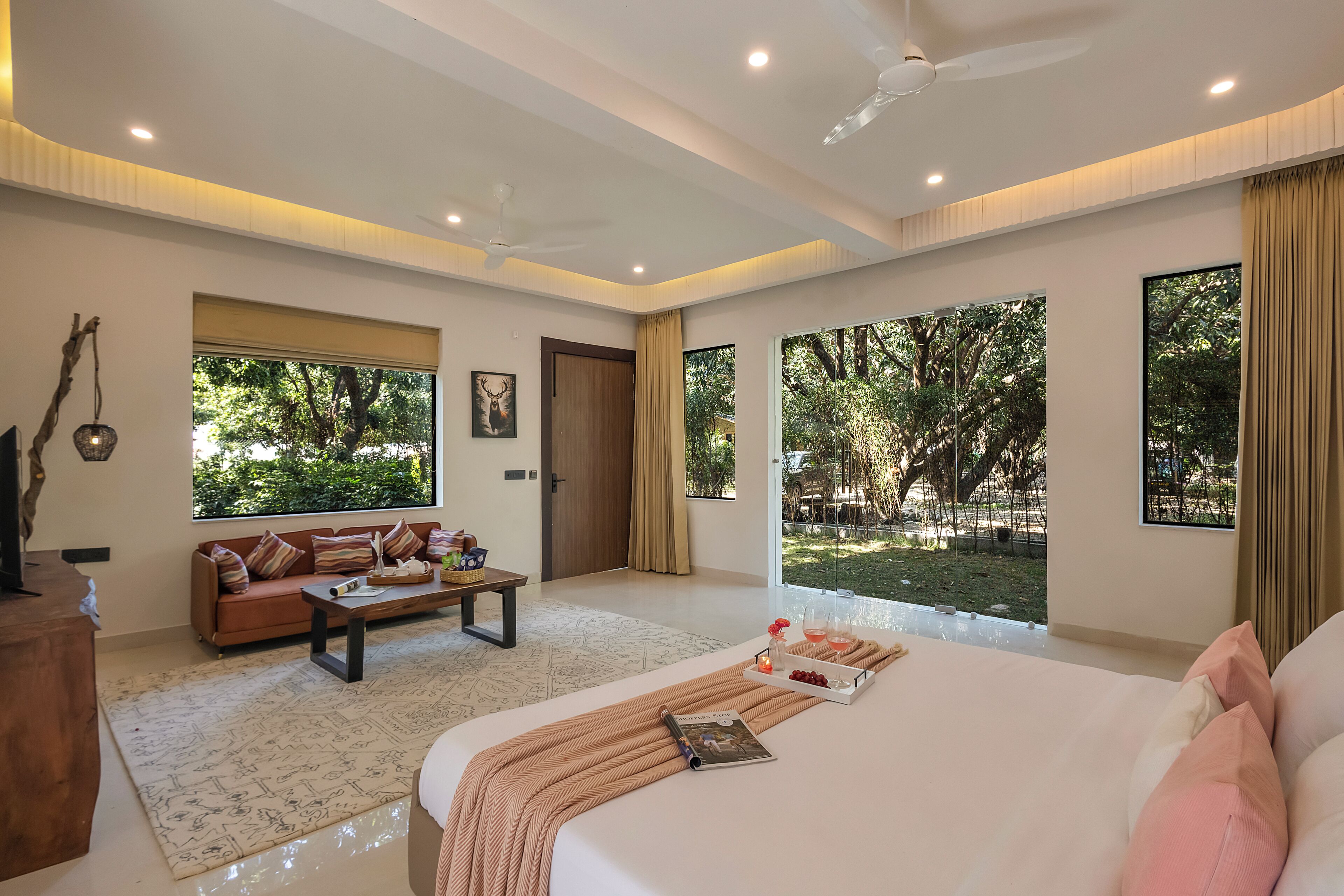 A spacious bedroom with a large bed, a sofa, a coffee table, and a view of the outdoors.