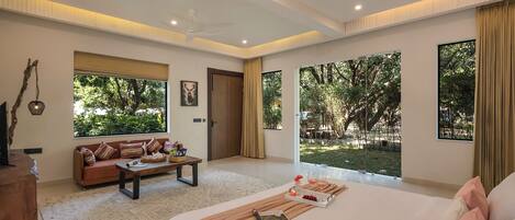 A spacious bedroom with a large bed, a sofa, a coffee table, and a view of the outdoors.