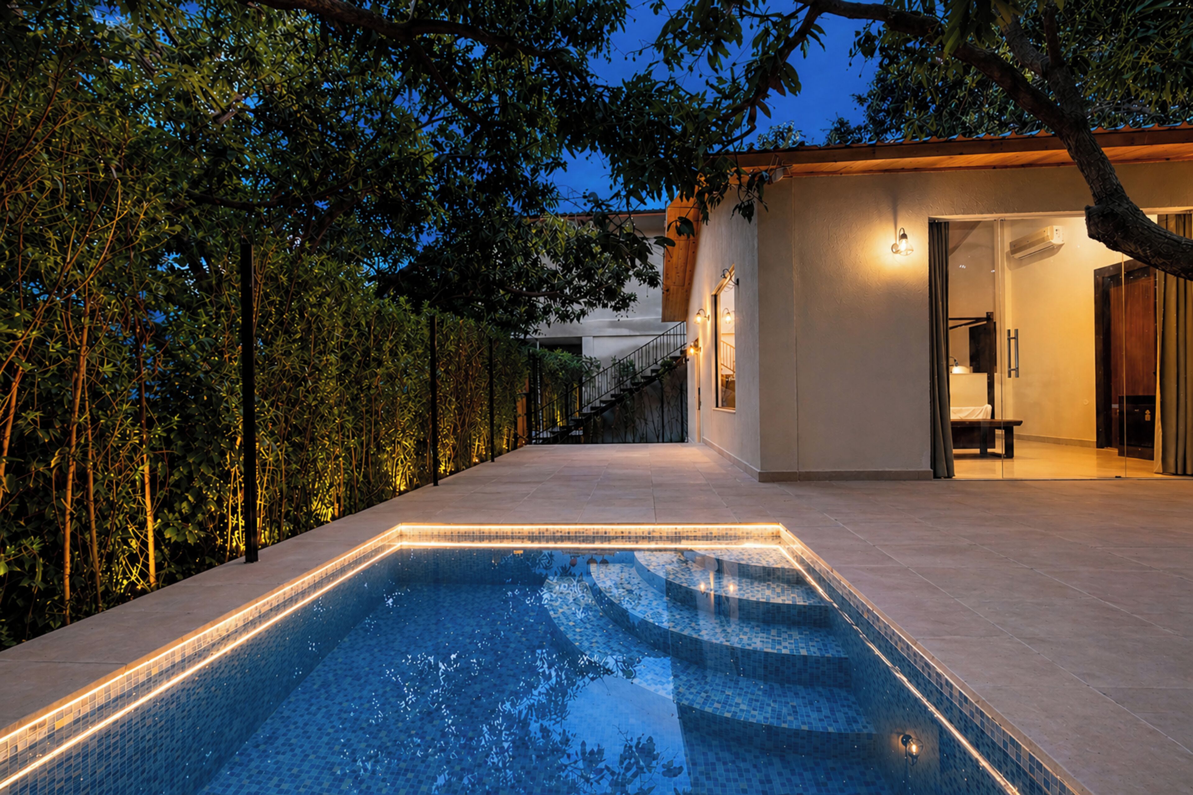 A swimming pool with a tiled edge, surrounded by a wooden deck and a hedge.