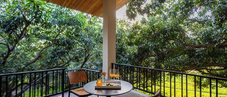 A covered outdoor seating area with a table, chairs, and a railing overlooking a lush garden.