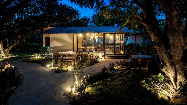A house with a glass facade, wooden deck, and outdoor seating area. - Sylvaara Suites by ELIVAAS Jim Corbett (Ramnagar)