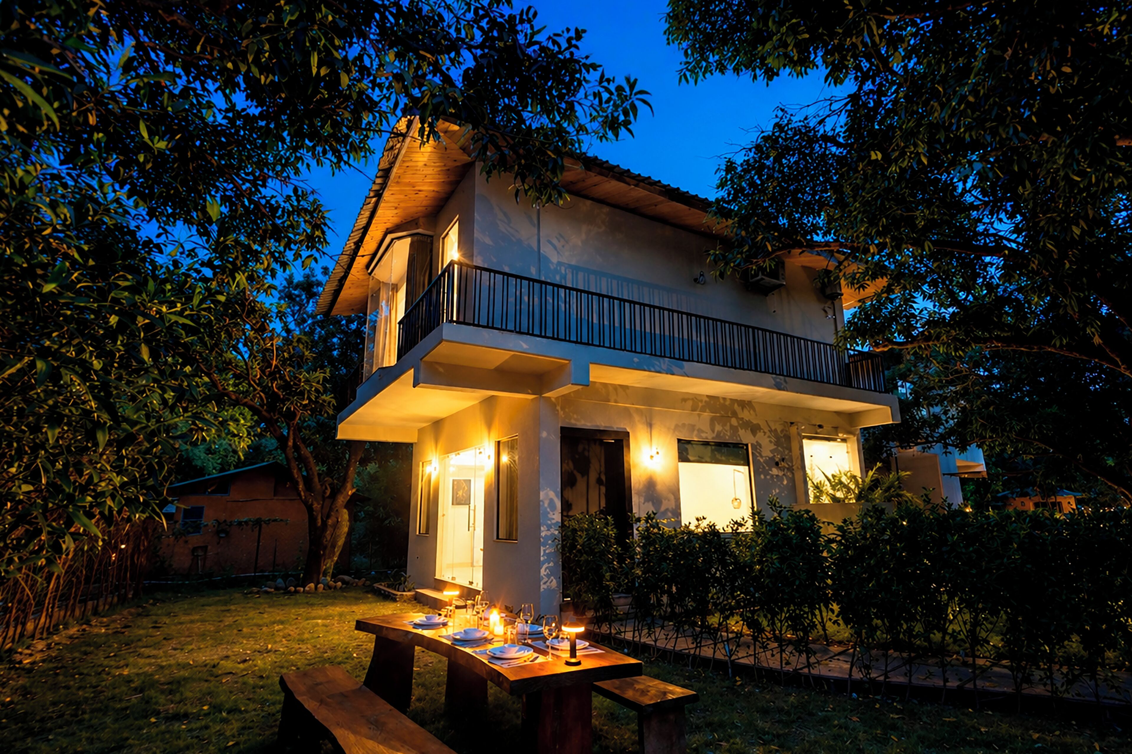 A two-story house with a balcony, a dining area with a table set for a meal, and a well-lit exterior.