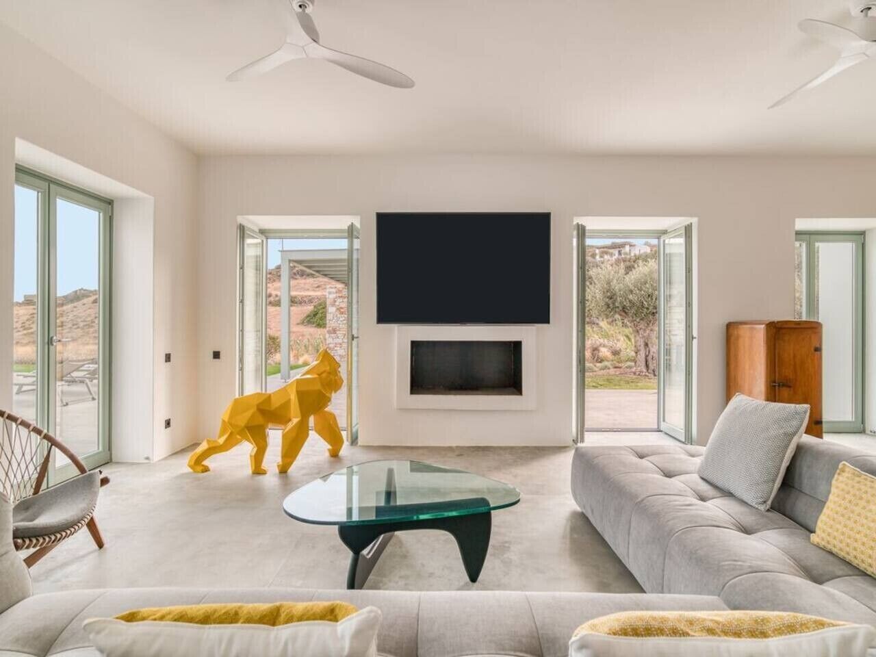 A spacious living room with a large sofa, a glass coffee table, and a flat-screen TV mounted on the wall.