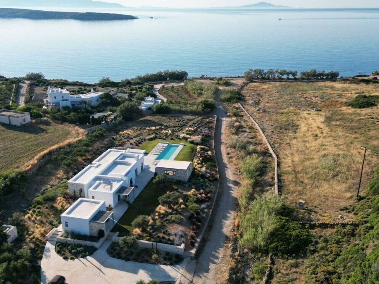 A modern villa with a swimming pool, surrounded by a natural landscape and a view of the sea.