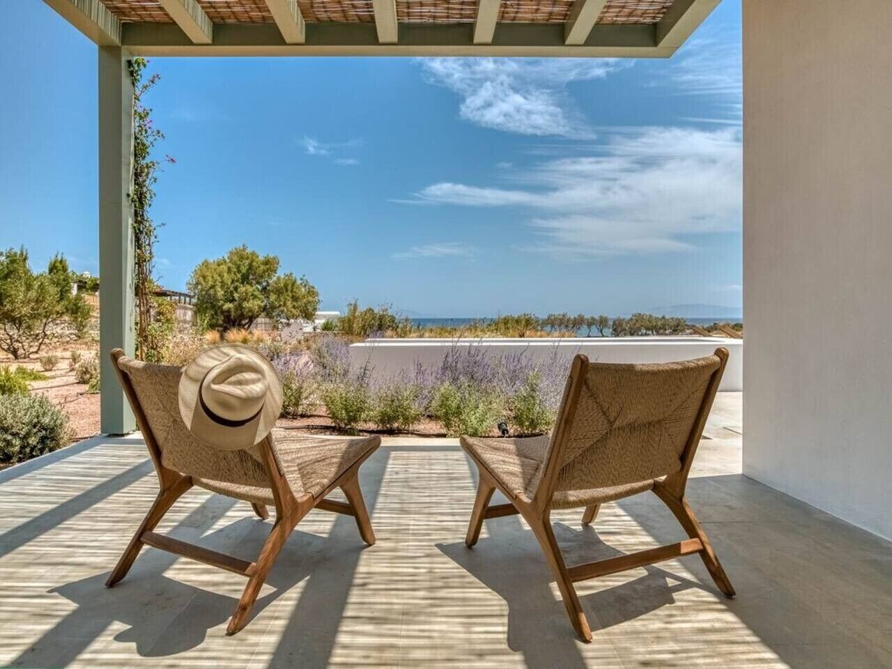 Two wicker chairs with a hat on one, a small table, and a view of the sea and desert landscape.
