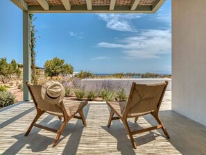 Zwei Korbstühle, einer mit Hut, ein kleiner Tisch und Blick auf Meer und Wüstenlandschaft.