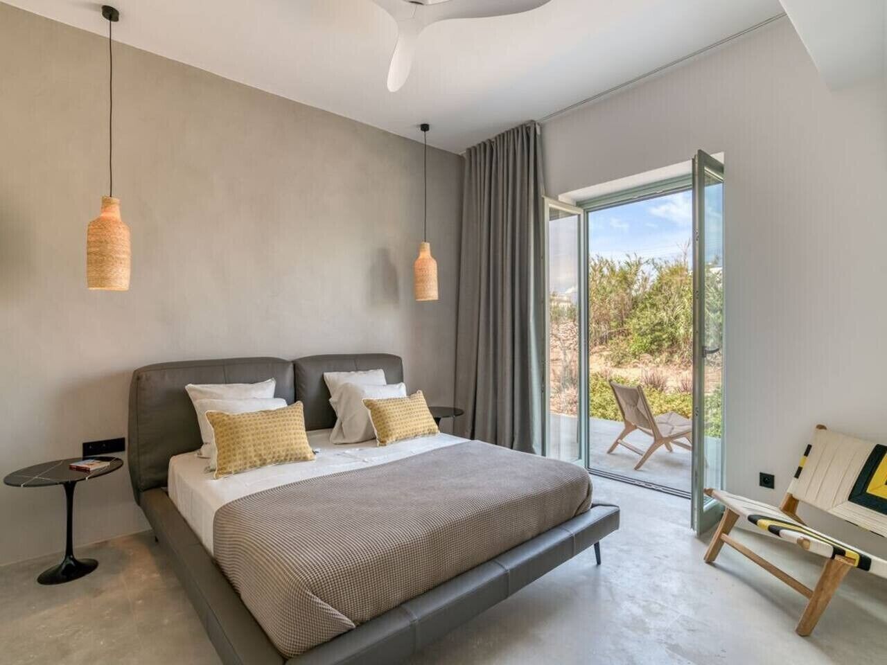 Ein modernes Schlafzimmer mit einem großen Bett, zwei Pendelleuchten, einem Nachttisch und Blick ins Freie.