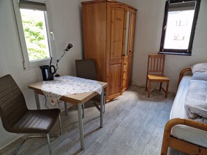A room with a wooden wardrobe, a table with a floral tablecloth, two chairs, a bed, and a window. - Bright, quietly located room, -2-, -close to the city in approx. 2 km- (Koblenz)