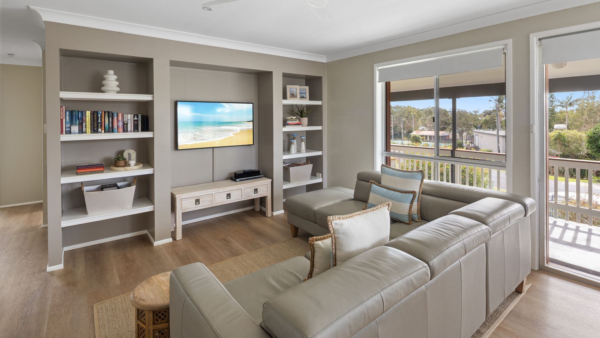 A living room with a sofa, TV, bookshelf, and a balcony with a view.