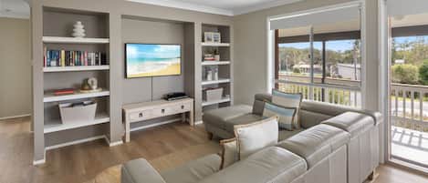 A living room with a sofa, TV, bookshelf, and a balcony with a view.