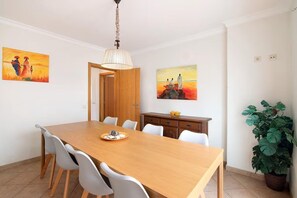 Ein Essbereich mit Holztisch, weißen Stühlen, einer Chandelierleuchtre und zwei Bildern an den Wänden.